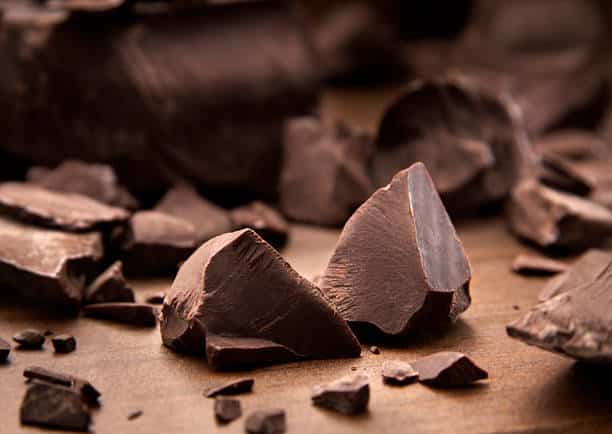 Pieces of dark chocolate spread out on a wooden background.
